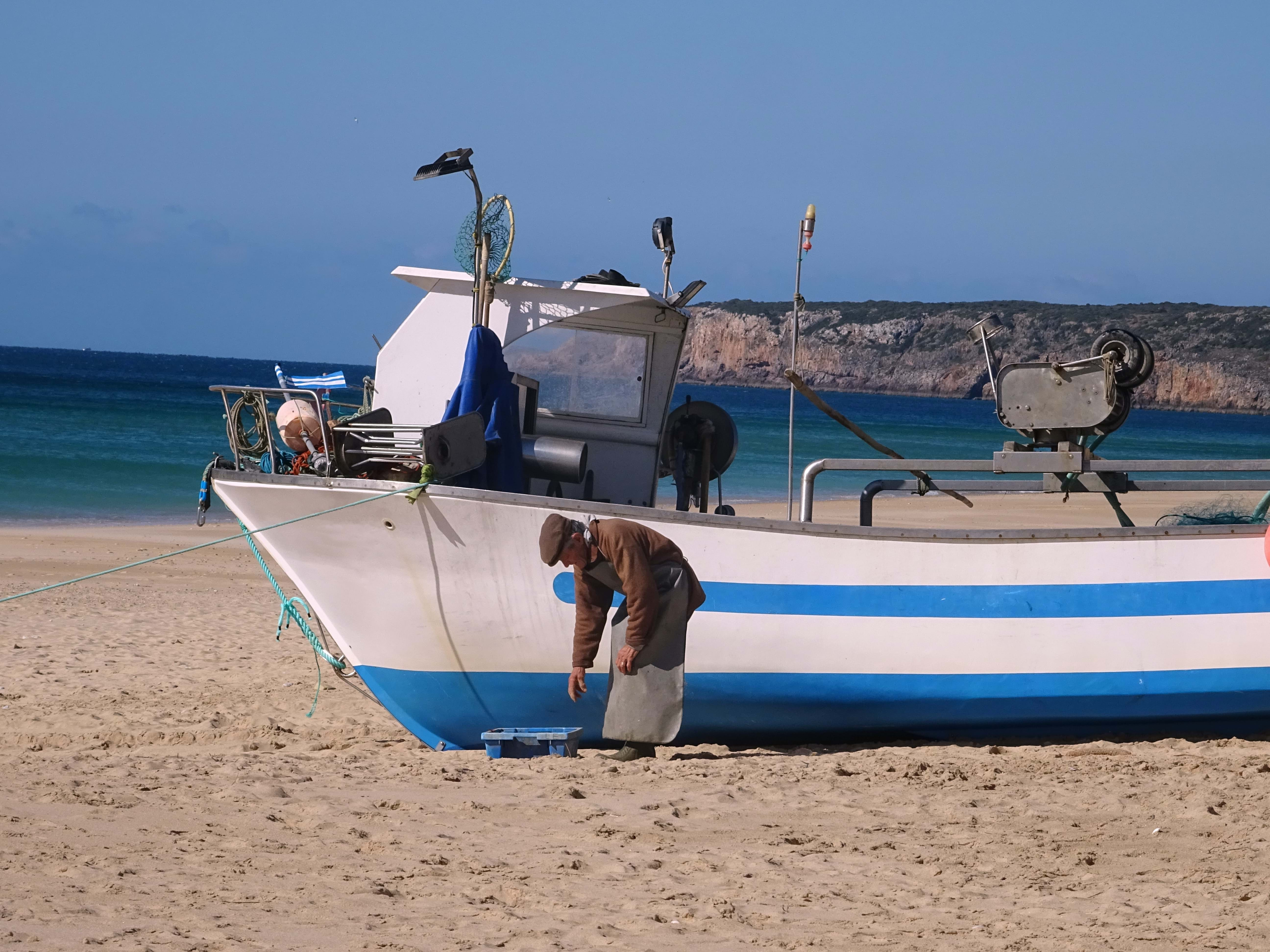 A fishing boat placed at the beach during low tide with an old man looking after it.